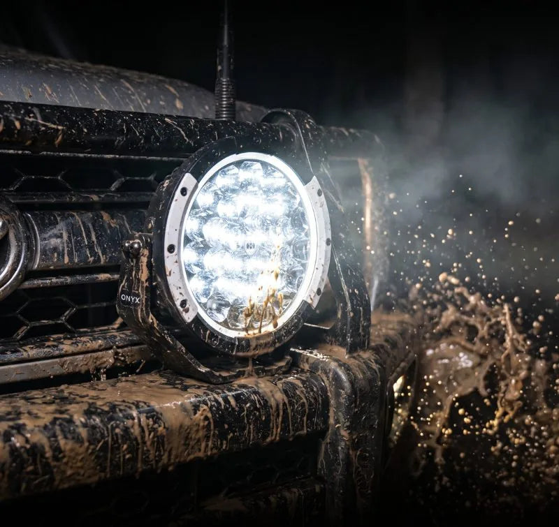 A TB-9 driving light lit up on a mud-covered bull bar at night